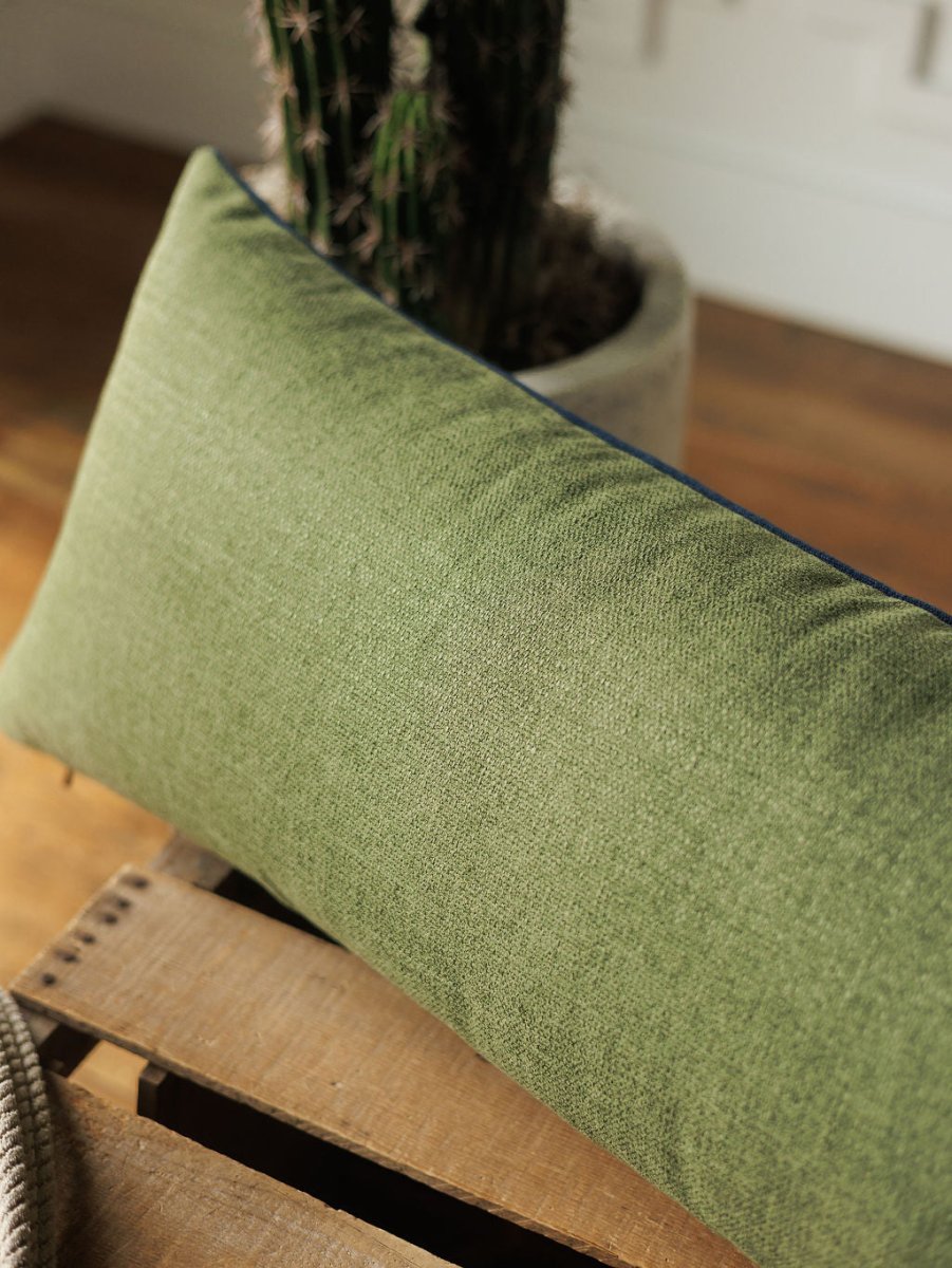The Presidio Lumbar Pillow Cover in Midnight Navy from Savannah Sevens western life{&}style rests on a wooden surface, with a potted cactus in the background and sunlight illuminating the scene.