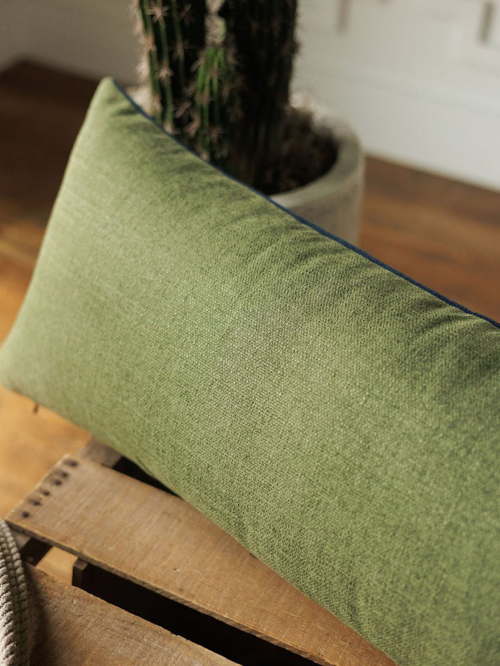 The Presidio Lumbar Pillow Cover in Midnight Navy from Savannah Sevens western life{&}style rests on a wooden surface, with a potted cactus in the background and sunlight illuminating the scene.