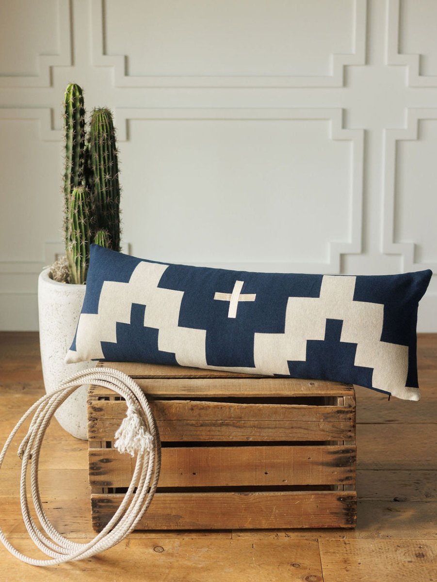 The Presidio Lumbar Pillow Cover {Midnight Navy} by Savannah Sevens western life{&}style features a navy and cream geometric Southwest design, displayed on a wooden crate with a potted cactus and rope, against a white decorative wall.