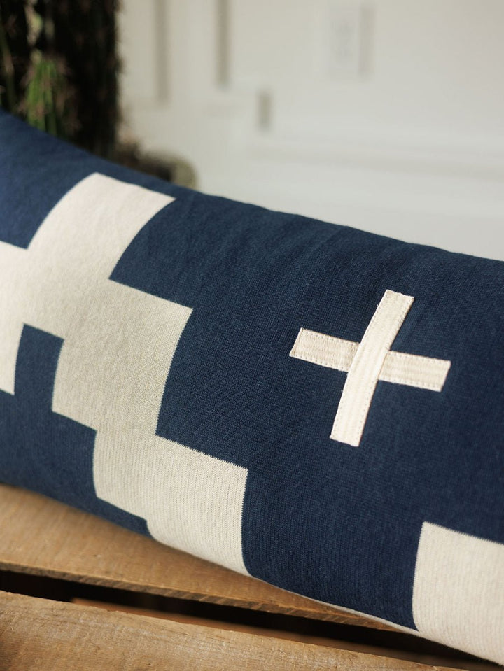 The Presidio Lumbar Pillow Cover {Midnight Navy} by Savannah Sevens western life{&}style features large geometric cream shapes and a stitched cream “X” on a navy background, displayed on wood with a blurred backdrop.