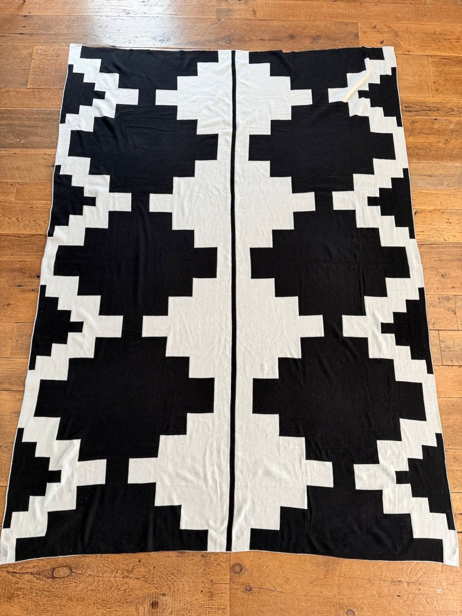 The Presidio Throw Blanket {B & W} by Savannah Sevens western life{&}style features luxury soft micro knit with bold, symmetrical black and white geometric step-pattern and zigzag designs, displayed flat on a wooden floor.