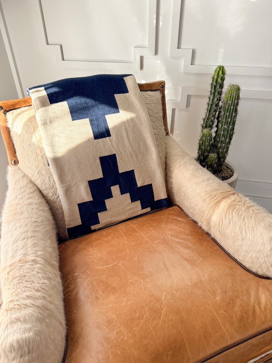A tan leather armchair is draped with a luxury soft micro knit faux fur throw and the Presidio Throw Blanket {Midnight Navy} by Savannah Sevens western life{&}style, while a tall potted cactus sits beside it against a sunlit white paneled wall.