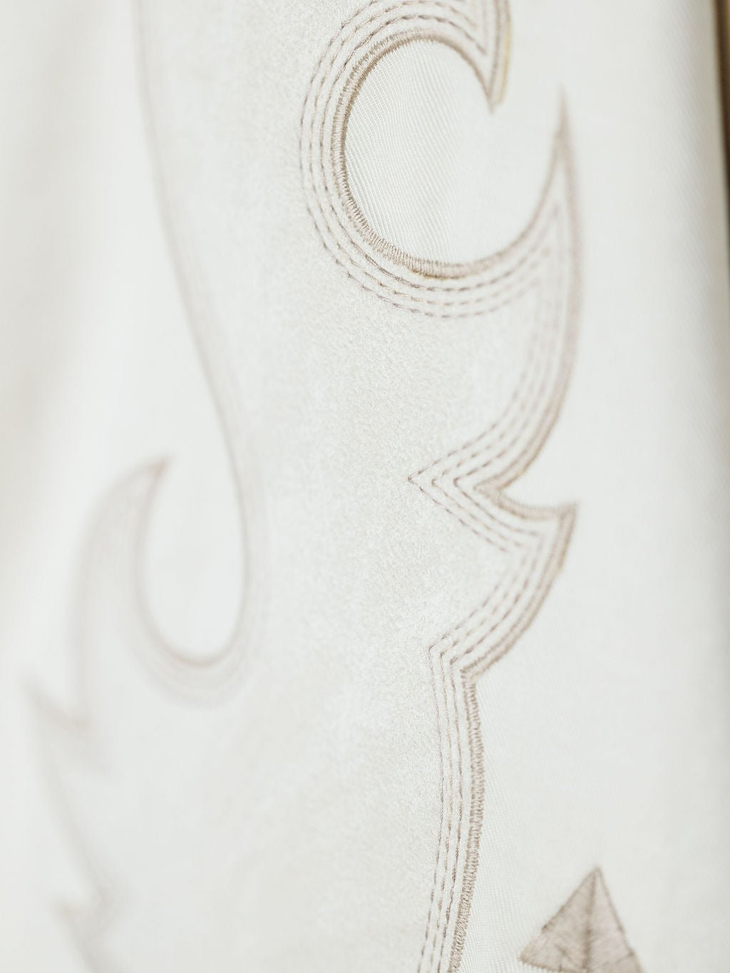 Close-up of the Questa Boot Stitch Jacket by Savannah Sevens western life{&}style, featuring soft beige faux suede with elegant, curved embroidery in a darker thread for a detailed and refined look.