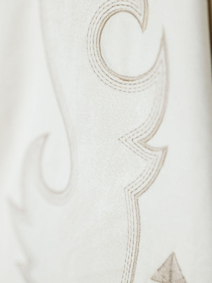 Close-up of the Questa Boot Stitch Jacket by Savannah Sevens western life{&}style, featuring soft beige faux suede with elegant, curved embroidery in a darker thread for a detailed and refined look.