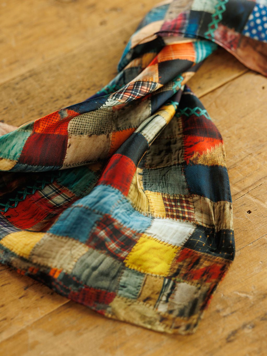 A Savannah Sevens western life&style Quilt Silk Scarf featuring a patchwork print of multicolored squares with plaid, polka dot, and solid patterns.