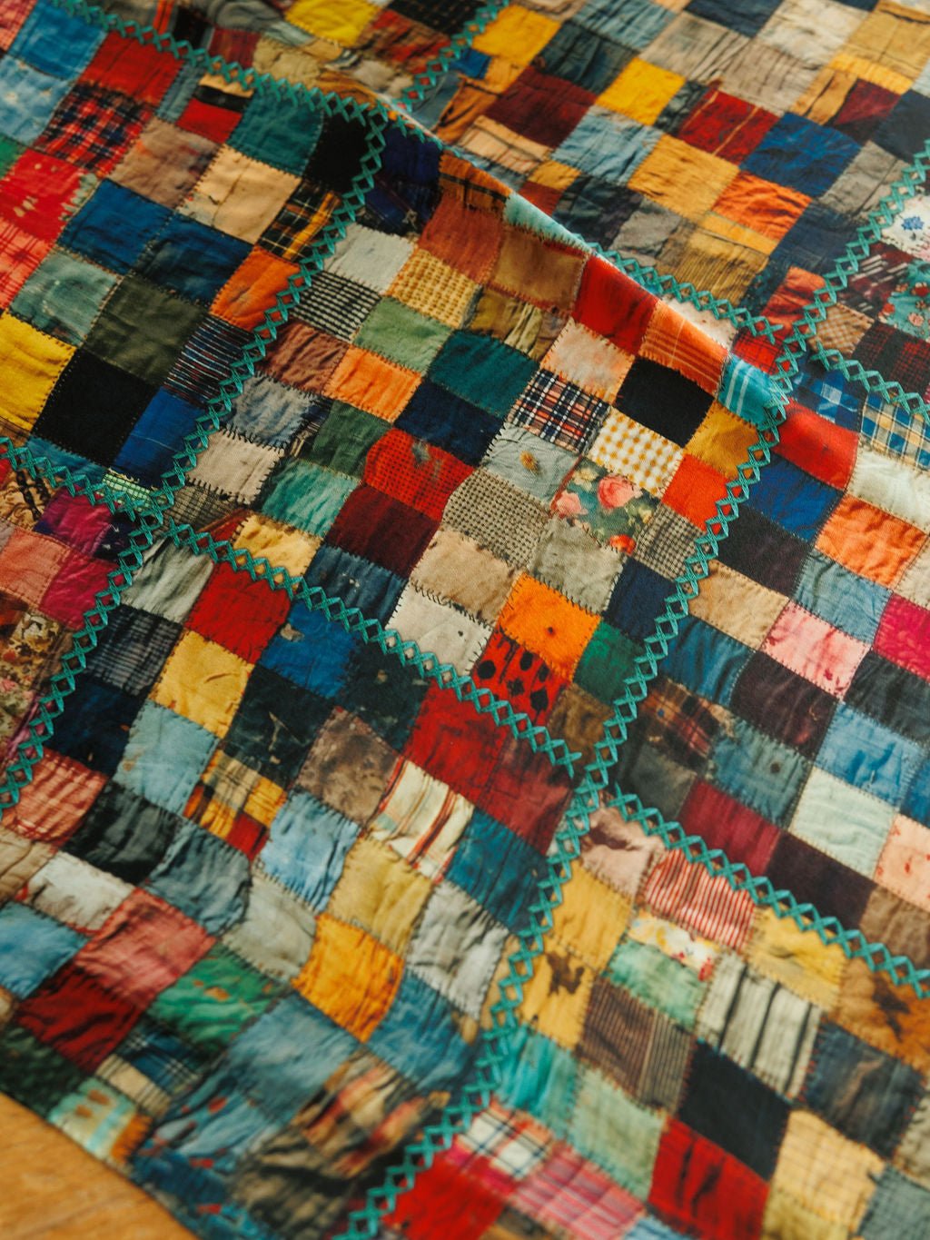 A Quilt Silk Scarf featuring a patchwork design of multicolored fabric squares joined by decorative teal zigzag stitching with a quilt print silk finish.