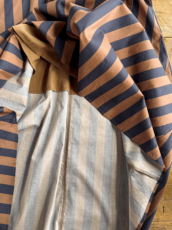 A close-up of the Ramona Striped Puff Sleeve Dress by Savannah Sevens western life{&}style displays its brown and navy diagonal stripes on the outside and beige and light blue vertical stripes on the inside, laid on a wooden surface.