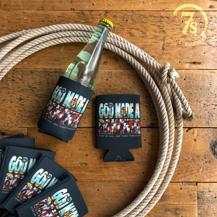 A Savannah Sevens western life{&}style Rancher Koozie with “God Made A...” and cowboy and cattle illustrations, slipped on a glass bottle, sits on coiled rope beside other Savannah Sevens fundraiser koozies on wood.