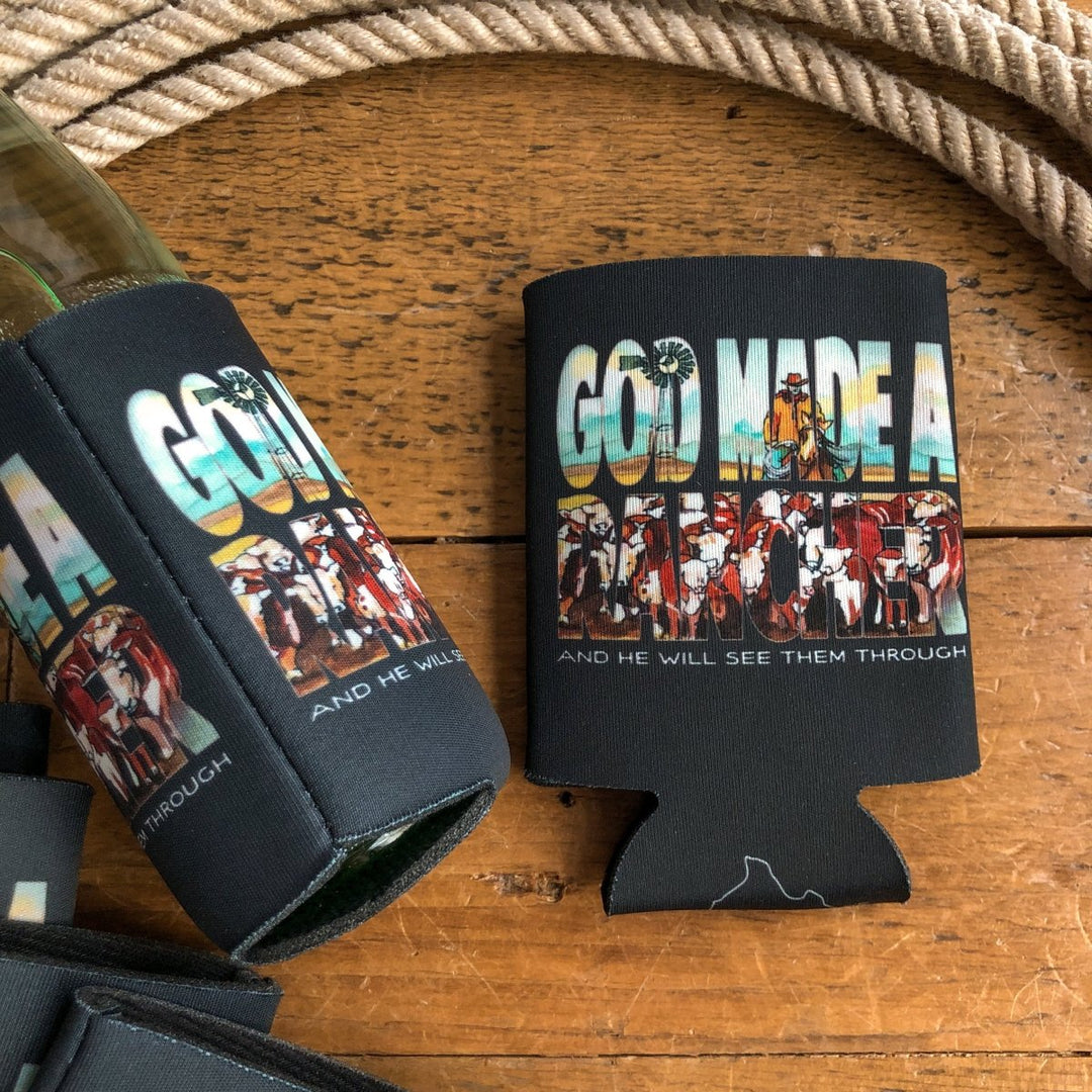 A black Rancher Koozie by Savannah Sevens western life{&}style sits on wood with rope nearby, featuring hand-drawn ranch scenes and cattle integrated in the text: "God Made A Rancher And He Will See Them Through.
