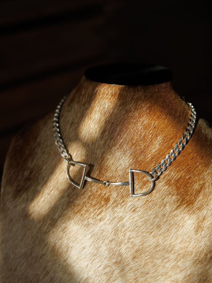 The Ranchero Necklace by Savannah Sevens western life{&}style, featuring sterling silver snaffle bit and D-shaped curb chain links, is shown on a brown and white cowhide mannequin bust in warm, soft light.