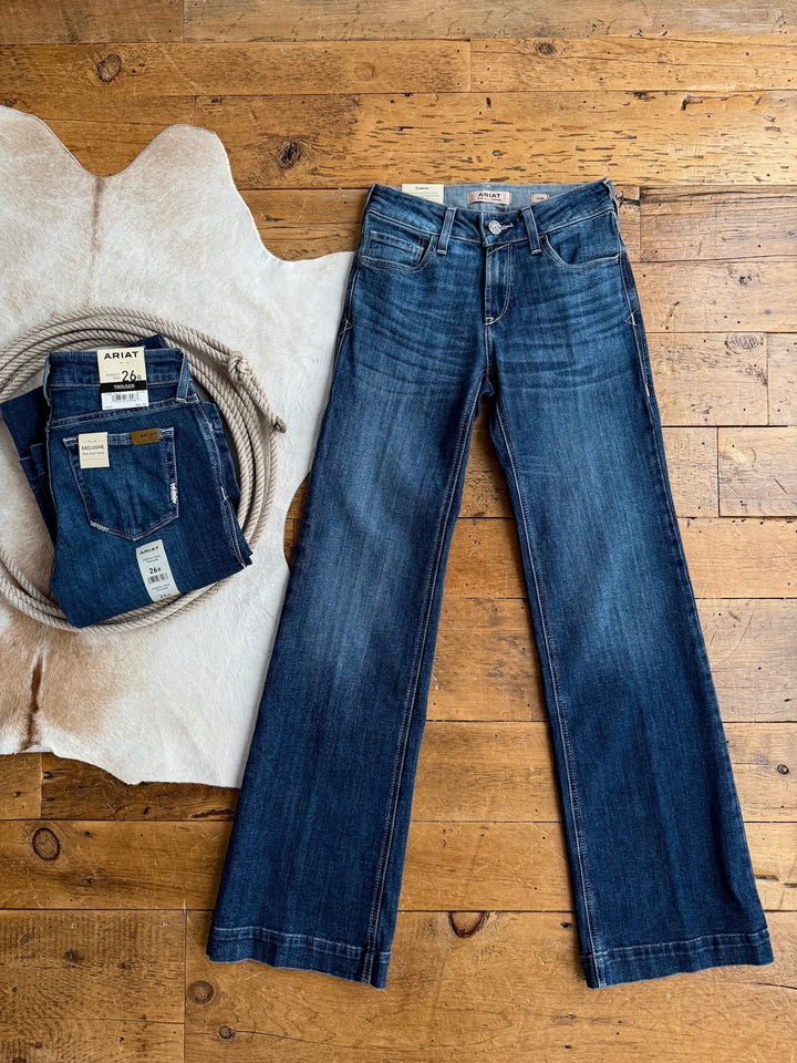 A pair of The Rawlins Perfect Rise Trouser Jean by Savannah Sevens western life{&}style in medium wash denim is laid flat next to a folded pair, both with tags, on a cowhide rug. Features a comfy no-gap waist for all-day comfort.