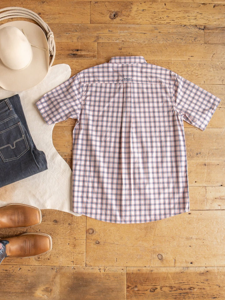 The Raymore Ariat Men's Plaid Button Up from Savannah Sevens western life{&}style is displayed flat on a wooden floor, accompanied by a beige cowboy hat, dark jeans, brown boots, and a light-colored cowhide rug. This shirt adds a timeless, classic vibe to any western-inspired look.
