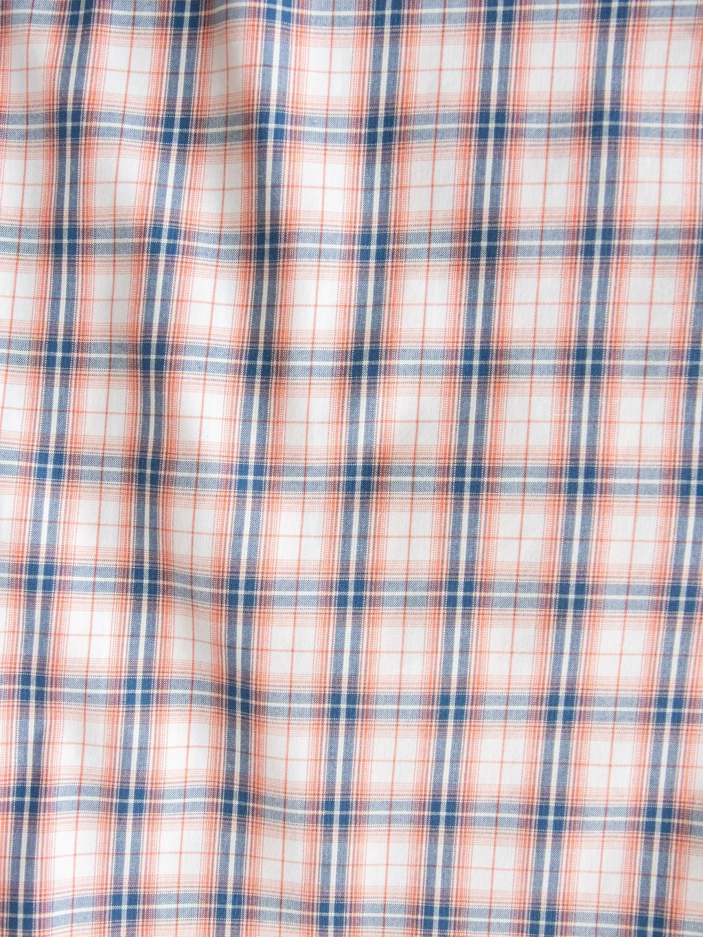 White fabric with a plaid pattern featuring thin orange and blue lines intersecting to form squares, and a subtly textured surface from slight wrinkling—perfect for the Raymore Ariat Men's Plaid Button Up by Savannah Sevens western life{&}style.