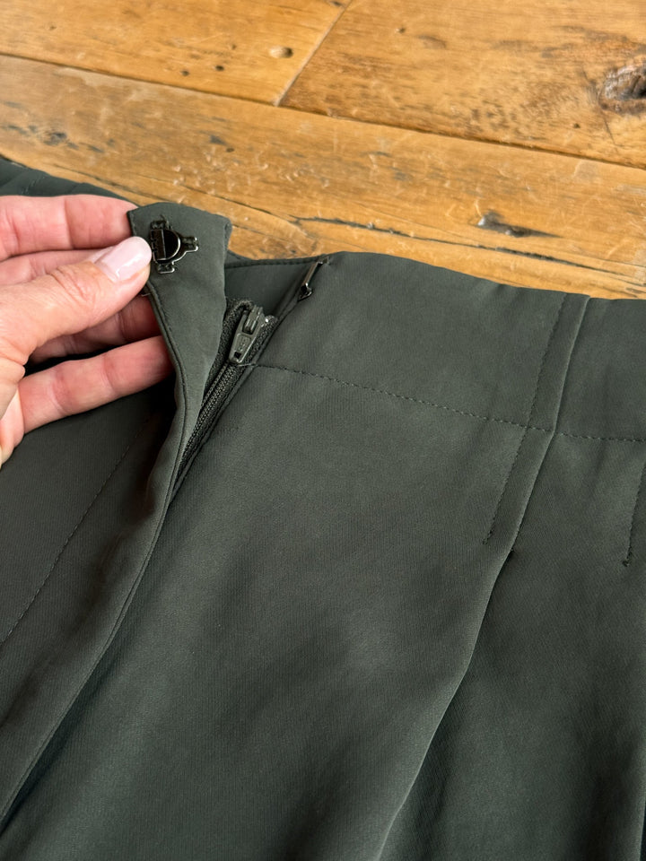 A hand holds open the waistband of the Revillo Charcoal Olive Blazer Set pants by Savannah Sevens western life{&}style, revealing a zipper and hook-and-eye closure against a wooden background.