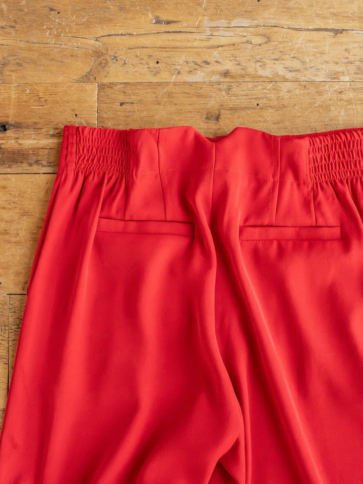 The Revillo Red Blazer Set by Savannah Sevens western life{&}style features bright red high-waisted pants with elastic waistbands, shown laid flat on a wooden surface to display their smooth fabric texture and two back welt pockets.