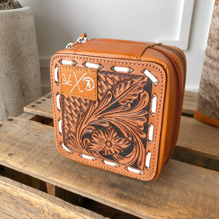 The Rialto Tooled Leather Mini Travel Jewelry Case by Savannah Sevens western life{&}style features intricate floral and basketweave designs, white stitching, and a subtle embossed logo—a stylish cowhide pouch for your essentials.