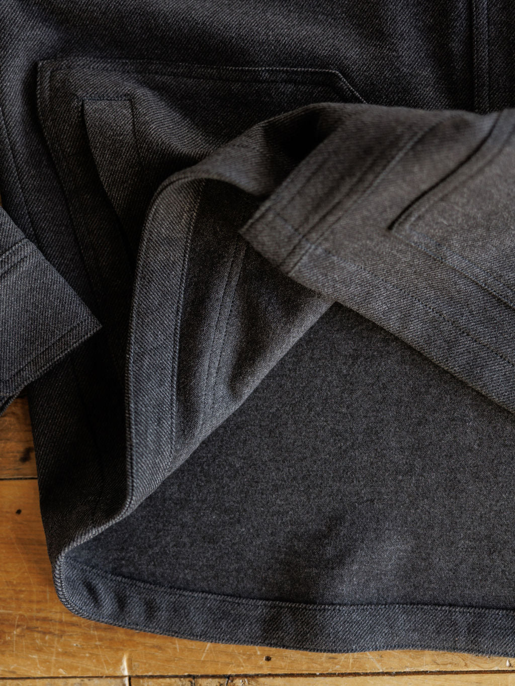 A close-up of the Richford Ariat Men's Charcoal Jacket by Savannah Sevens western life{&}style, folded on a wooden surface with visible hem, sleeve, and stitching details.