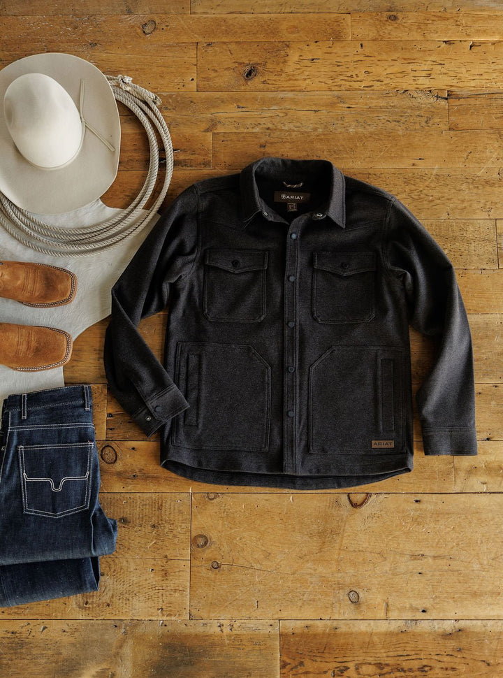A Richford Ariat Men's Charcoal Jacket from Savannah Sevens western life{&}style is displayed on a wooden floor beside a white cowboy hat, brown boots, a gray shirt, and folded blue jeans.