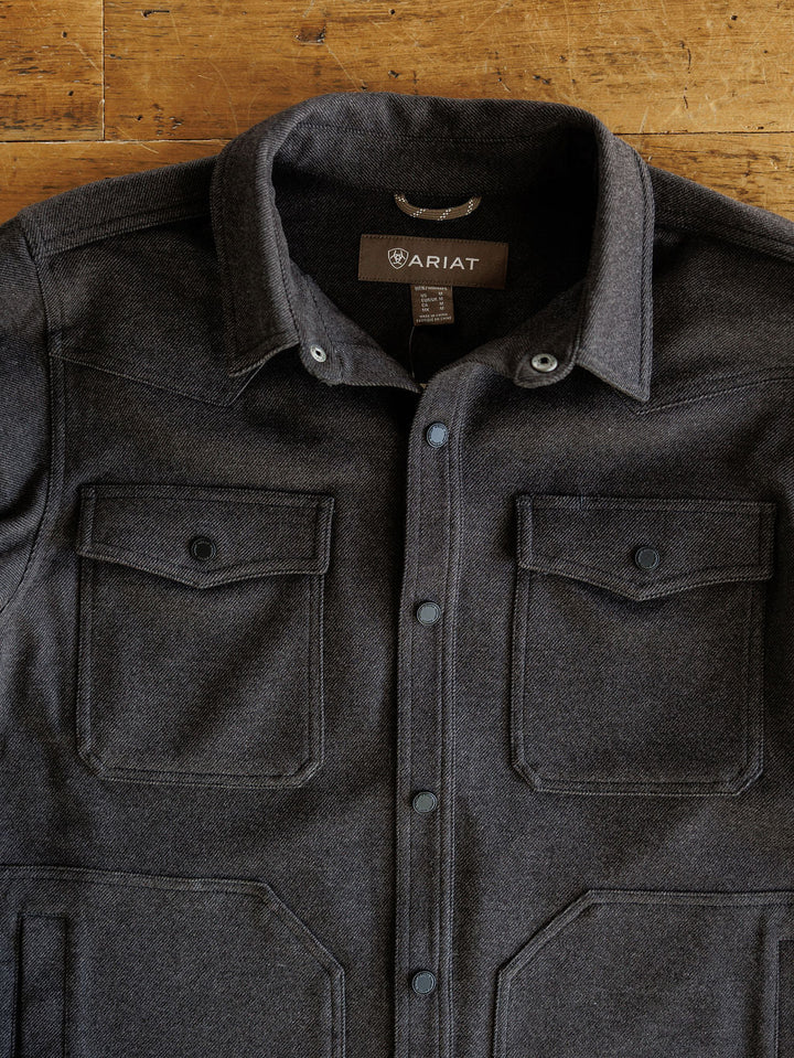 The Richford Ariat Men's Charcoal Jacket by Savannah Sevens western life{&}style, featuring snap buttons and two front chest pockets, lies flat on a wooden surface. This heather charcoal jacket is both stylish and functional for any occasion.
