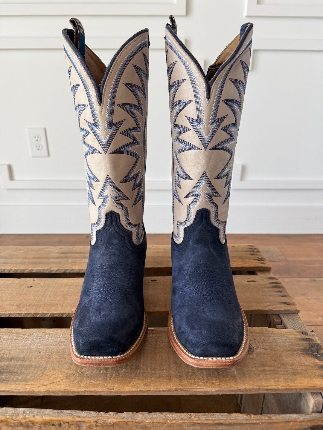 A pair of Rose Hill Navy Western Leather Boots by Savannah Sevens western life{&}style, featuring decorative stitching and a cutter toe, stand upright on a wooden pallet against a white wall. Boots by HYER. 