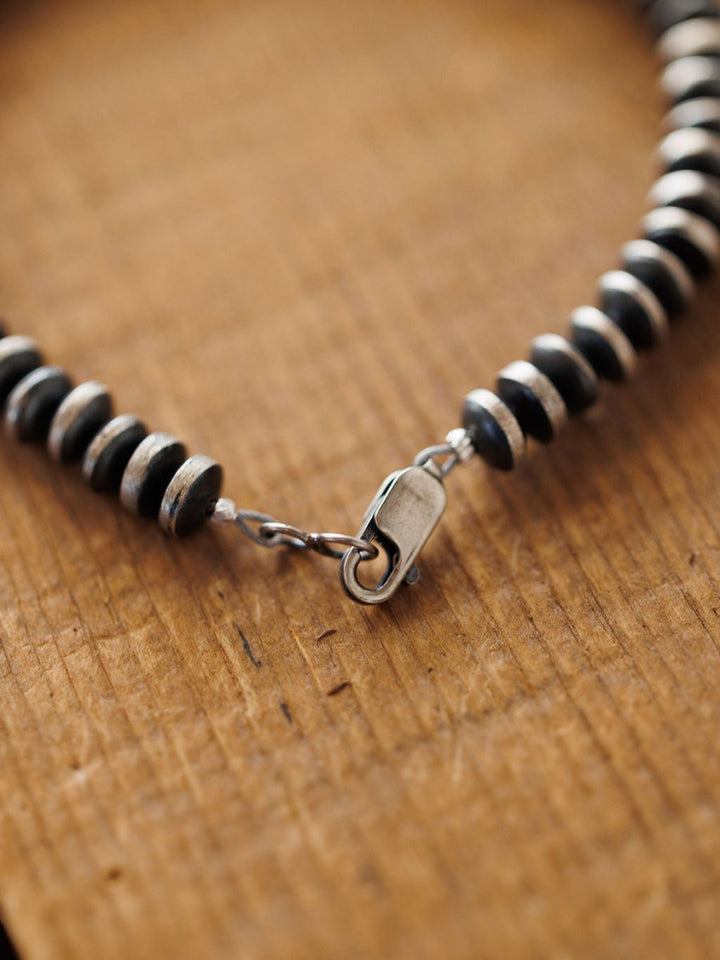 Close-up of the Rowlett Bracelet by Savannah Sevens western life{&}style, with alternating black and sterling silver 4mm rondelle beads and a silver clasp, displayed on textured wood.