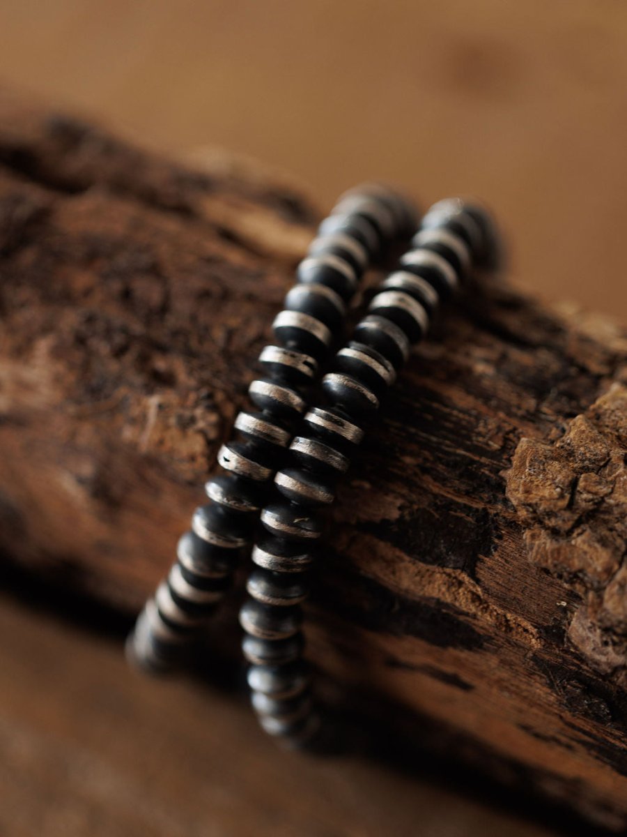 Close-up of two Rowlett Bracelets by Savannah Sevens western life{&}style, featuring 4mm black and sterling silver Navajo pearl rondelle beads with a rustic oxidized finish, draped over textured brown wood and highlighting their metallic details.