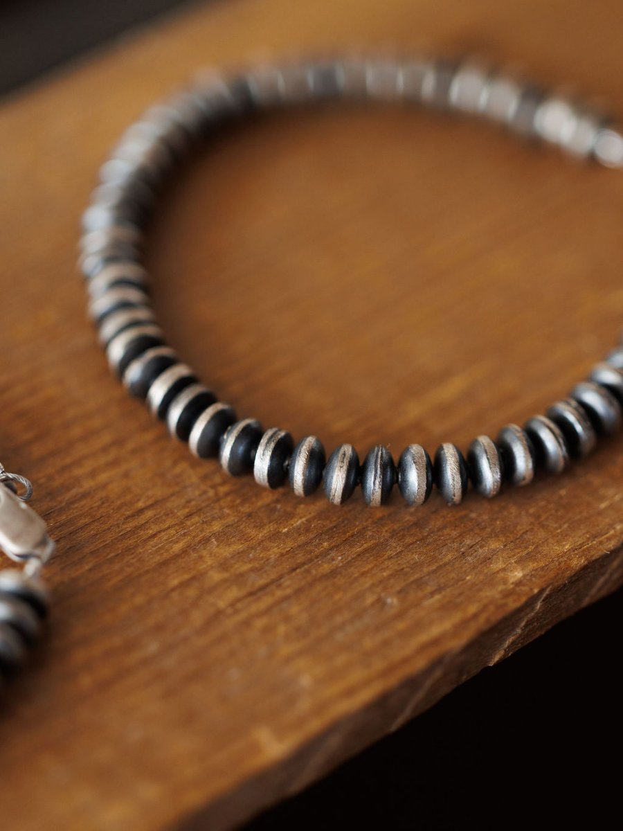 A close-up of the Rowlett Bracelet by Savannah Sevens western life{&}style shows alternating black and sterling silver 4mm rondelle beads resting on wood, evenly spaced and forming a partial circle.