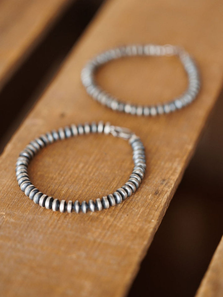 Two Rowlett Bracelets by Savannah Sevens western life{&}style, made with 4mm sterling silver rondelle beads in a Navajo pearl style, are displayed on wood—one sharply in focus in front, the other blurred in the background.