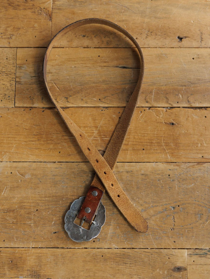The Ruidoso Belt by Savannah Sevens western life{&}style is displayed in a loose loop on wood, showcasing its brown leather strap, scalloped sterling silver Navajo buckle, and multiple sizing holes.