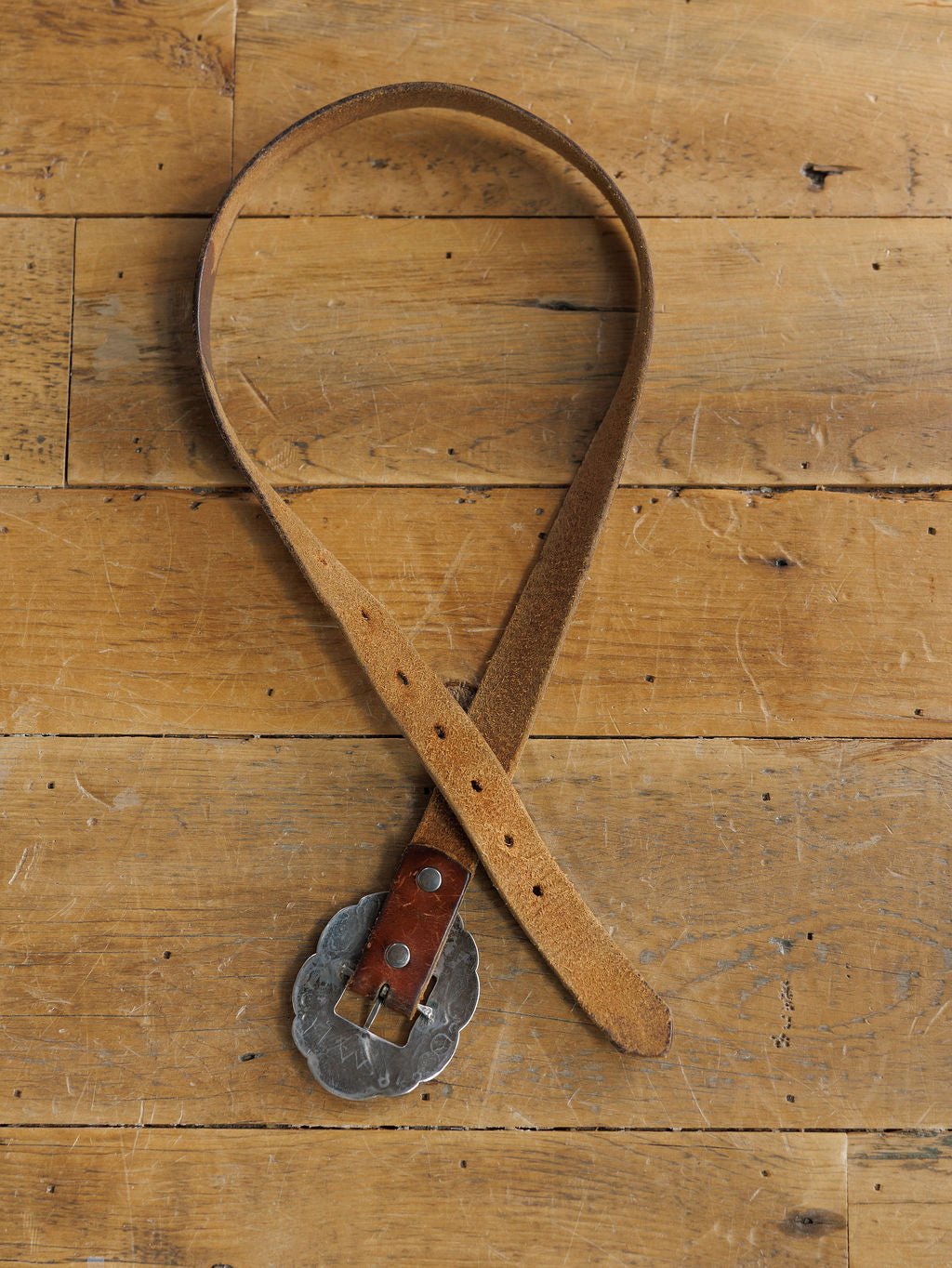 The Ruidoso Belt by Savannah Sevens western life{&}style is displayed in a loose loop on wood, showcasing its brown leather strap, scalloped sterling silver Navajo buckle, and multiple sizing holes.