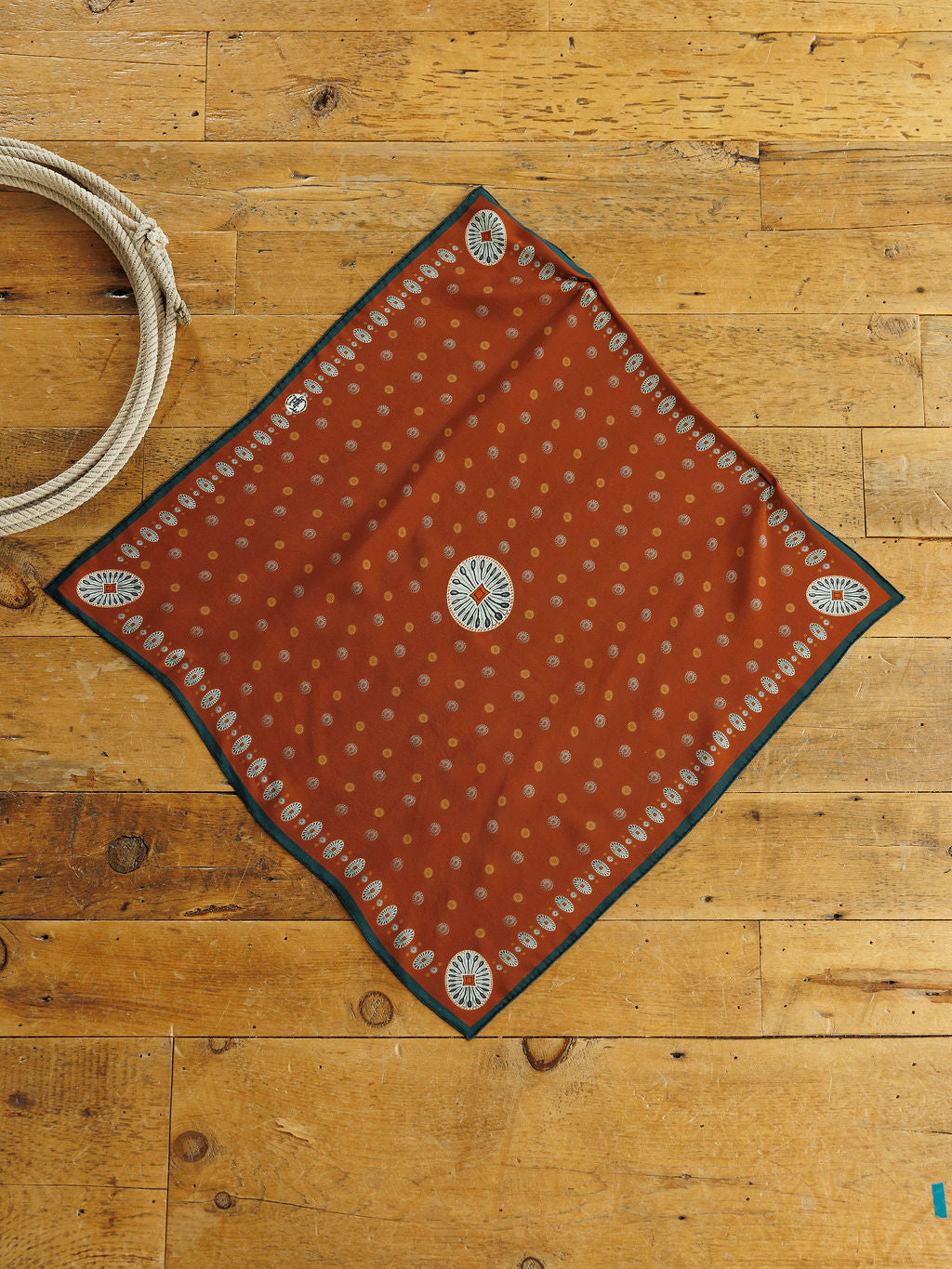 San Miguel Silk Scarf, a square rust orange neck scarf with a repeating cream dot pattern and a decorative floral border in a Southwest style.