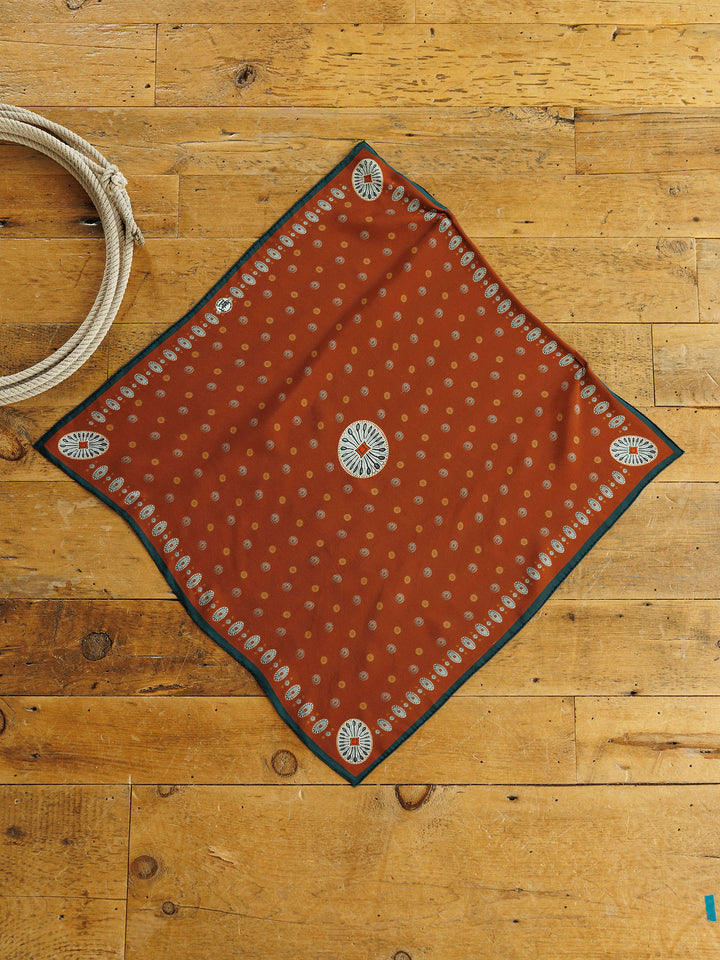 San Miguel Silk Scarf, a square rust orange neck scarf with a repeating cream dot pattern and a decorative floral border in a Southwest style.
