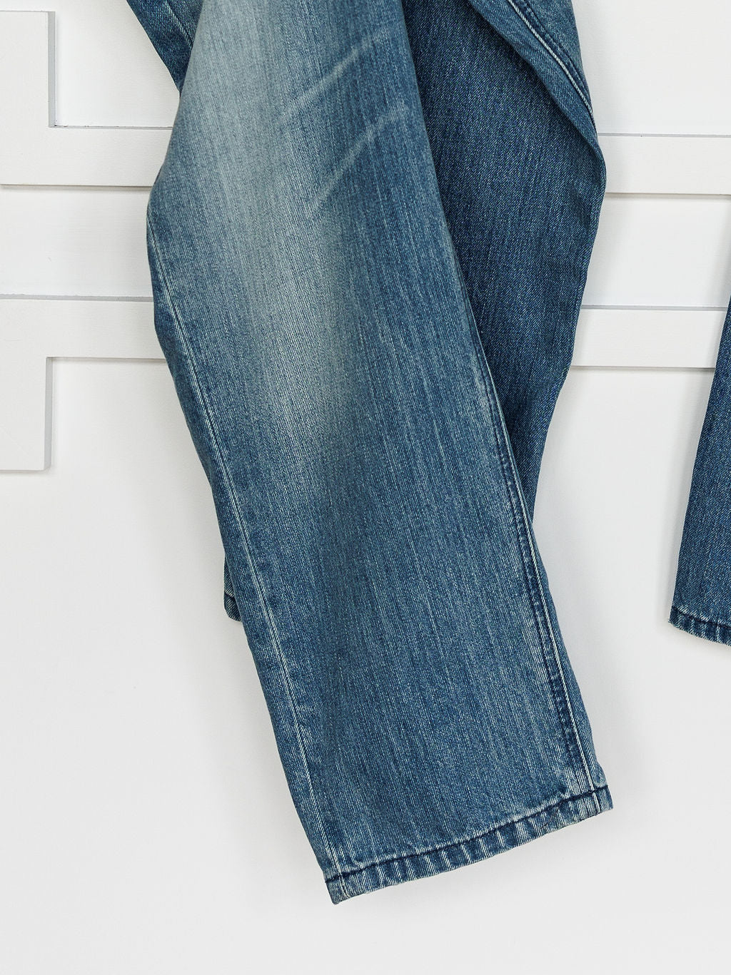 A close-up of Ariat’s The Truett High Rise Relaxed Straight Leg Jean in medium wash, draped over a white surface to showcase its faded texture and seam details.