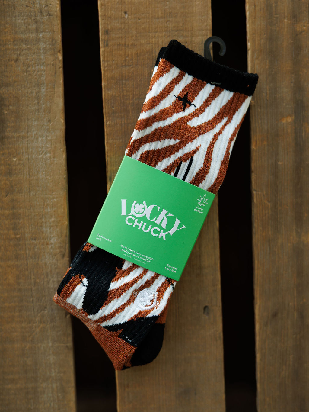 A pair of Maverick Crew Socks by Savannah Sevens western life{&}style, featuring brown, black, and white zebra stripes in an odor-fighting hemp blend, wrapped in a green Lucky Chuck label and displayed on a wooden surface.
