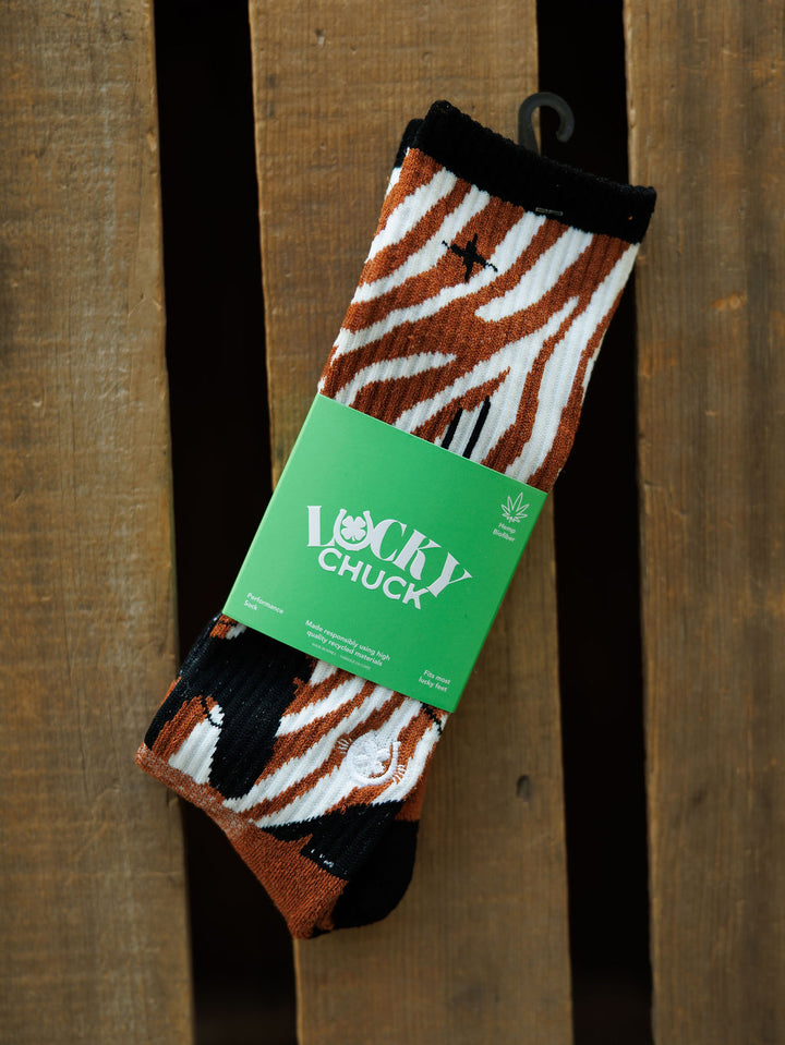 A pair of Maverick Crew Socks by Savannah Sevens western life{&}style, featuring brown, black, and white zebra stripes in an odor-fighting hemp blend, wrapped in a green Lucky Chuck label and displayed on a wooden surface.