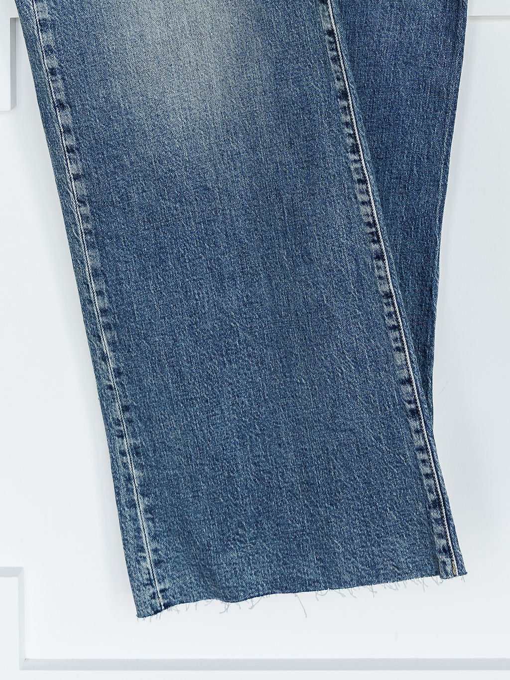 Close-up of the lower legs of The Leyden High Rise Wide Leg Jean by Savannah Sevens western life{&}style in medium wash denim, featuring a frayed, unfinished hem against a white background.