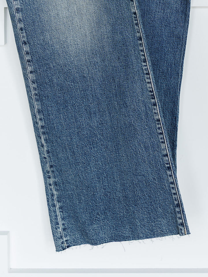 Close-up of the lower legs of The Leyden High Rise Wide Leg Jean by Savannah Sevens western life{&}style in medium wash denim, featuring a frayed, unfinished hem against a white background.