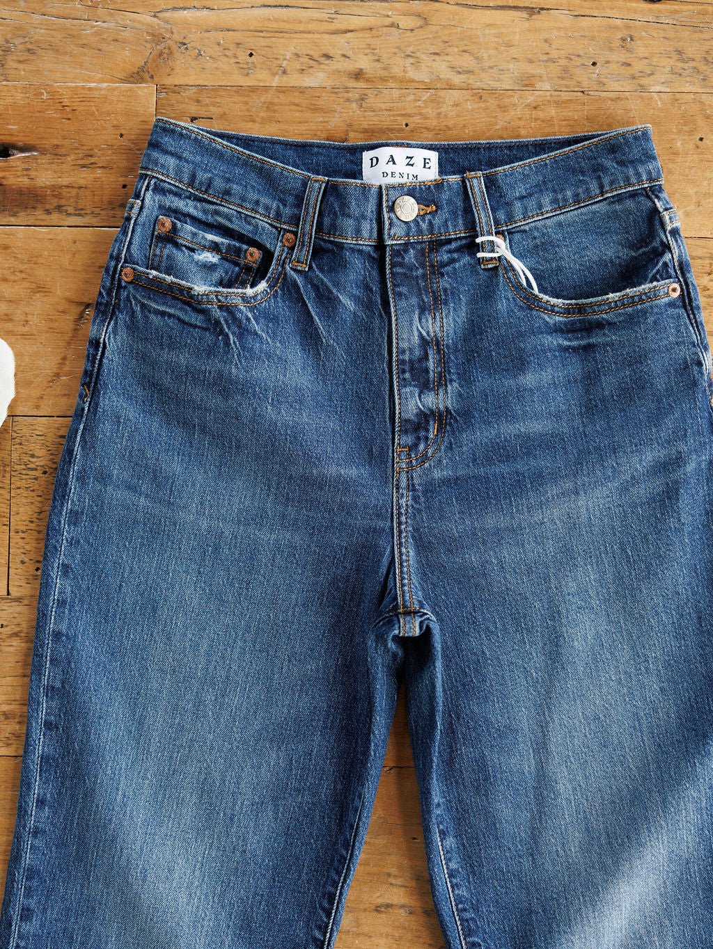 The Payton High Rise Relaxed Straight Leg Jean by Savannah Sevens western life{&}style, in blue, features a button fly, front pockets, and visible stitching, shown laid flat on a wooden surface.