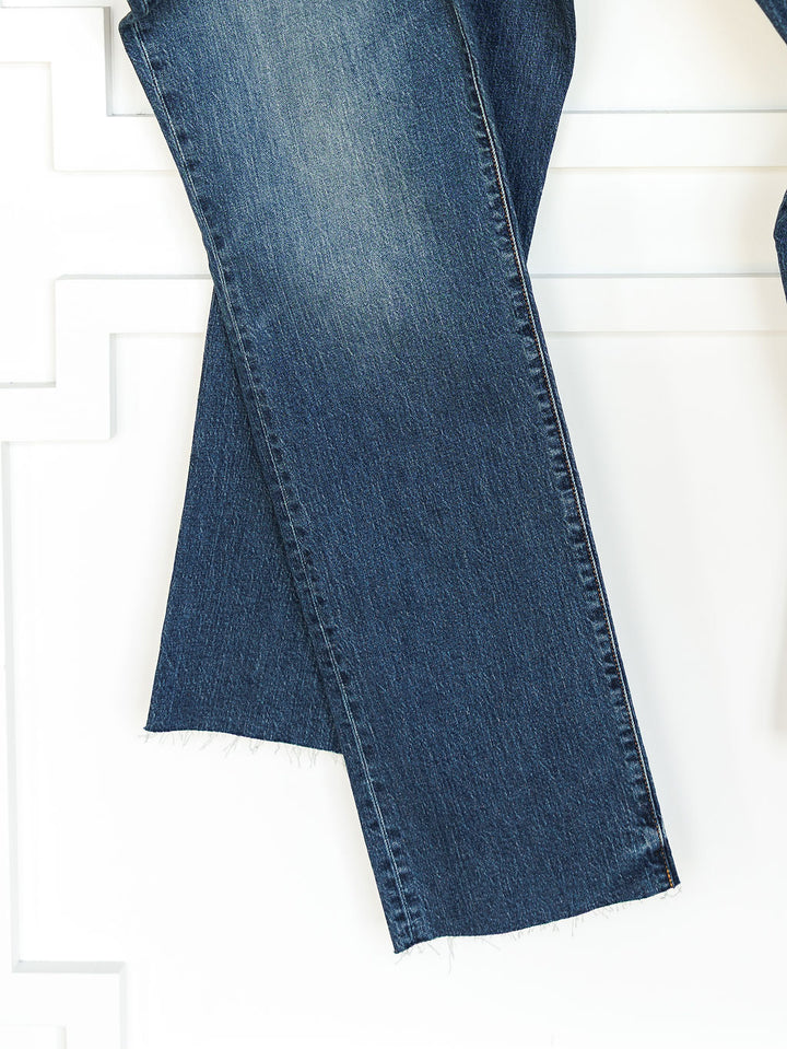 Two pant legs of medium dark wash denim, The Payton High Rise Relaxed Straight Leg Jean by Savannah Sevens western life{&}style, with a slight faded finish and raw hem are shown against a white background.