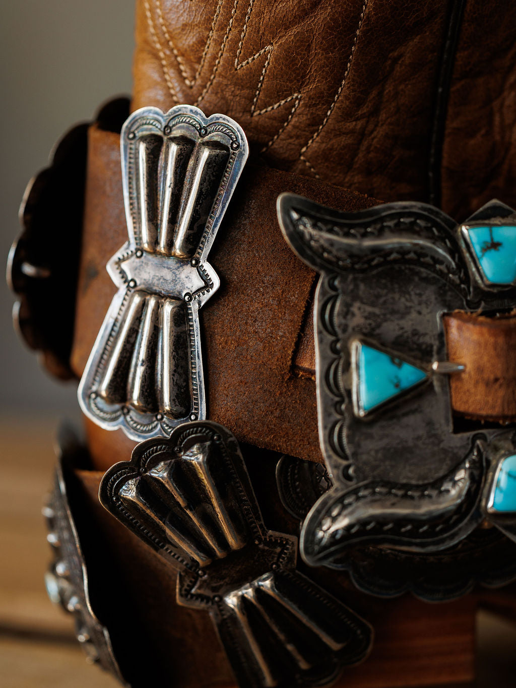 Close-up of Portales Belt by Savannah Sevens western life{&}style, a brown leather cowboy boot accessory adorned with vintage sterling silver and #8 Turquoise concho belt, featuring intricate engraved patterns.