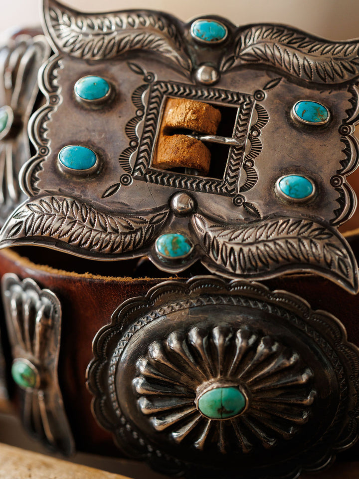 Close-up of the New Mexico Belt by Savannah Sevens western life{&}style, showcasing an ornate sterling silver buckle with intricate engravings and turquoise stones on a handmade leather strap.