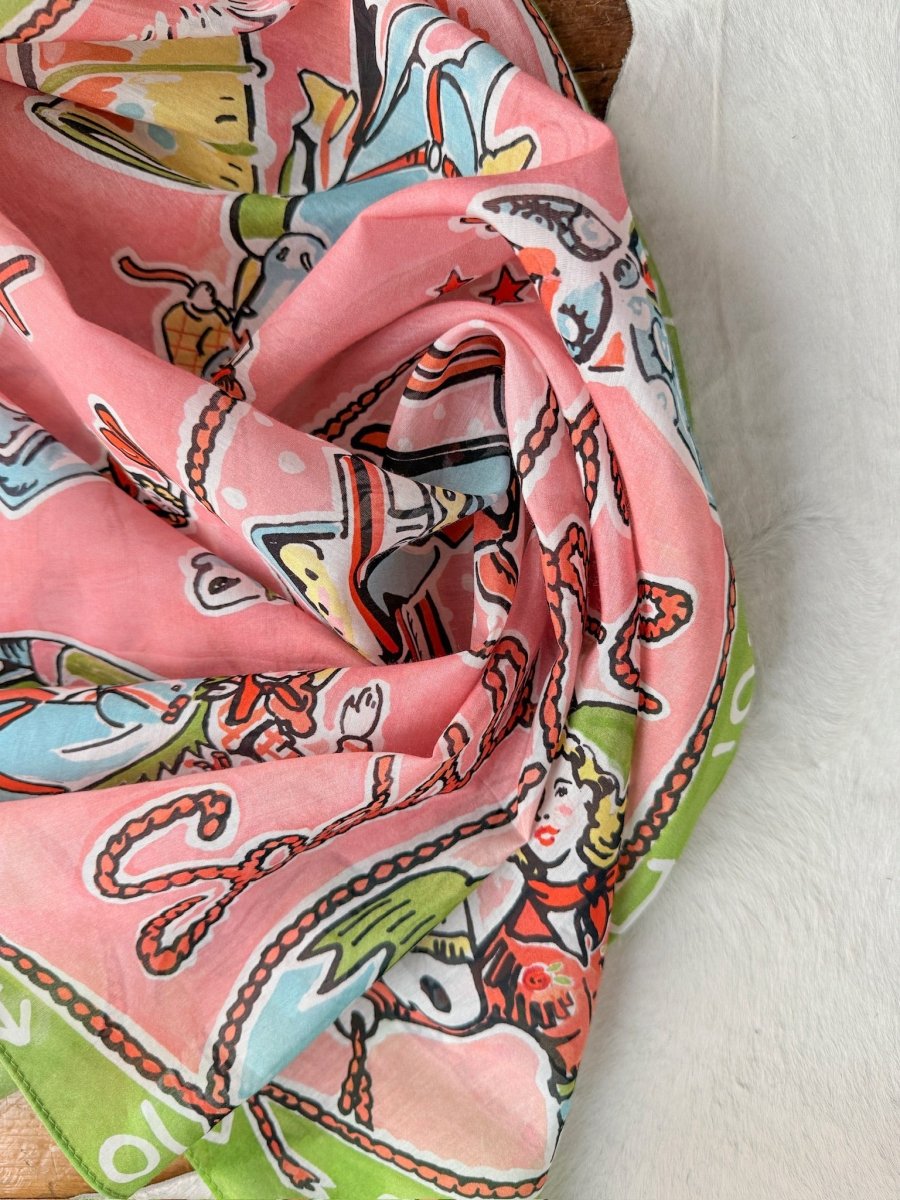 The Saddle Up Neck Scarf by Savannah Sevens western life{&}style features a whimsical illustrated design of a woman's face, sea creatures, and playful shapes in vibrant tones—styled with soft folds for a retro western vibe.