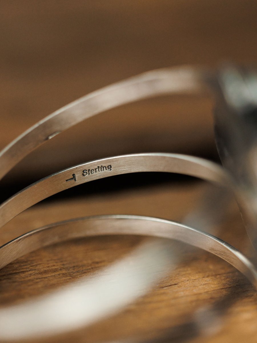 Close-up of the unique Sagola Cuff by Savannah Sevens western life{&}style, featuring "Sterling" stamped inside and resting on a wooden surface.