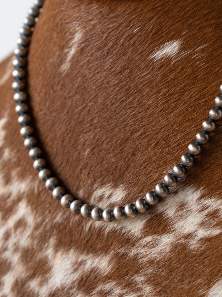 A close-up of the Saledo Navajo Pearl Necklace by Savannah Sevens western life{&}style, featuring 6mm sterling silver beads, displayed on a brown and white speckled cowhide surface.
