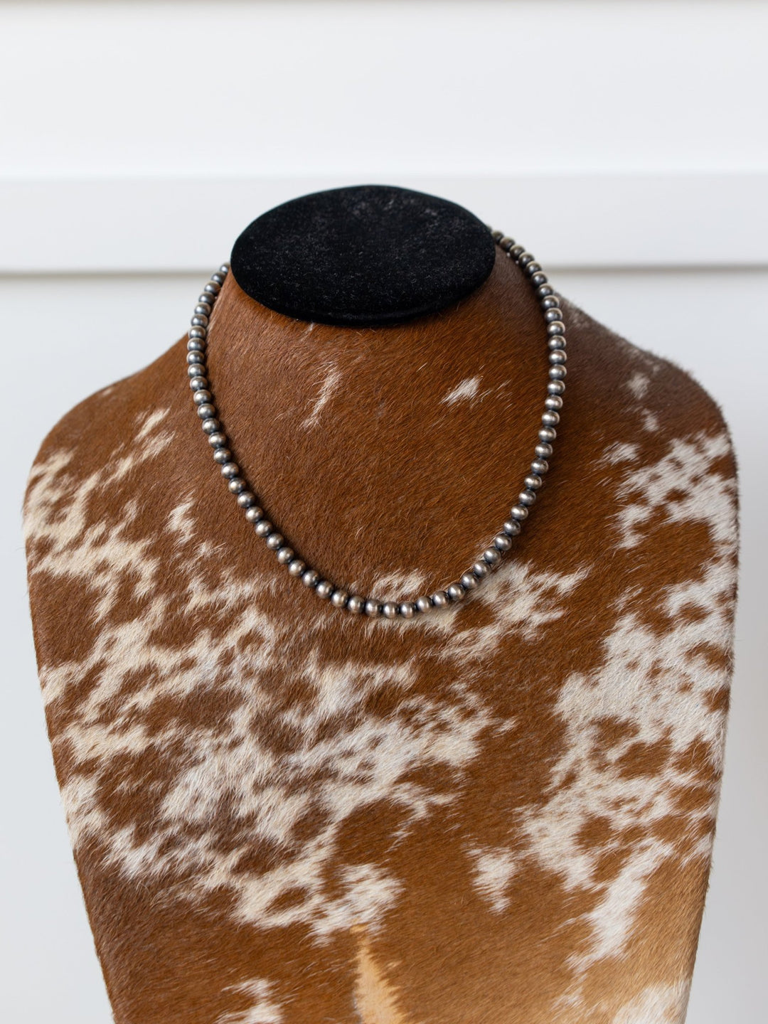 The Saledo Navajo Pearl Necklace by Savannah Sevens western life{&}style, featuring 6mm beads, is displayed on a cowhide-covered bust with a black velvet top against a white background.
