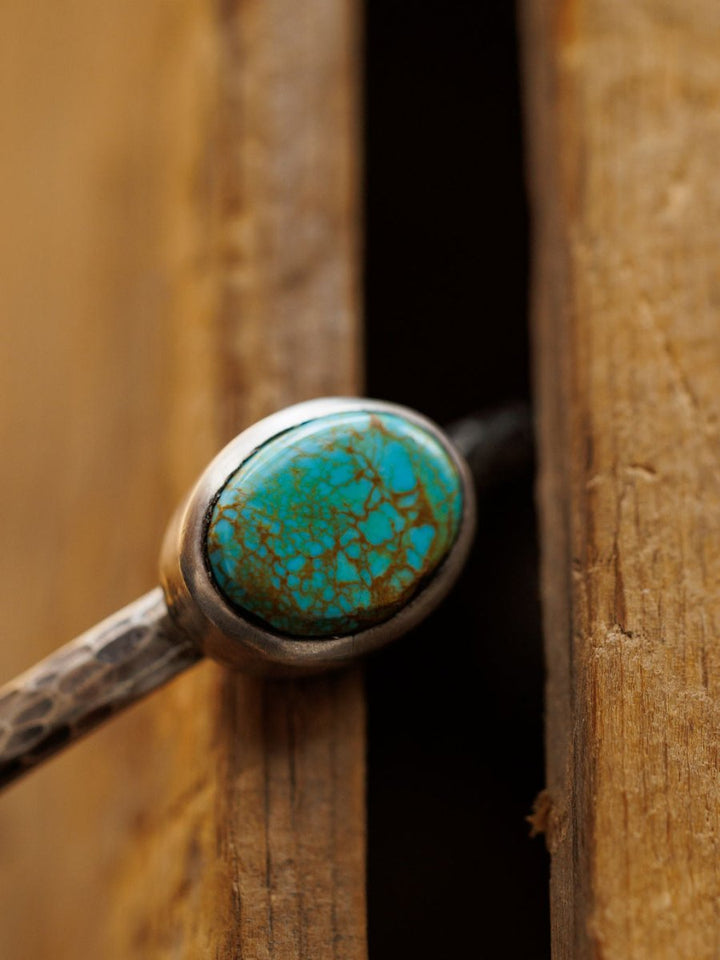 A close-up of the Salida Cuff by Savannah Sevens western life{&}style, showcasing an oval Kings Manassa turquoise stone with brown matrix, resting against a wooden edge.