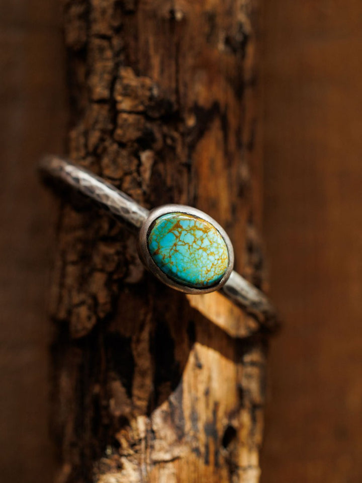 The Salida Cuff by Savannah Sevens western life{&}style—a hammered bracelet with a blue and gold marbled Kings Manassa turquoise stone—rests on textured, sunlit wood.