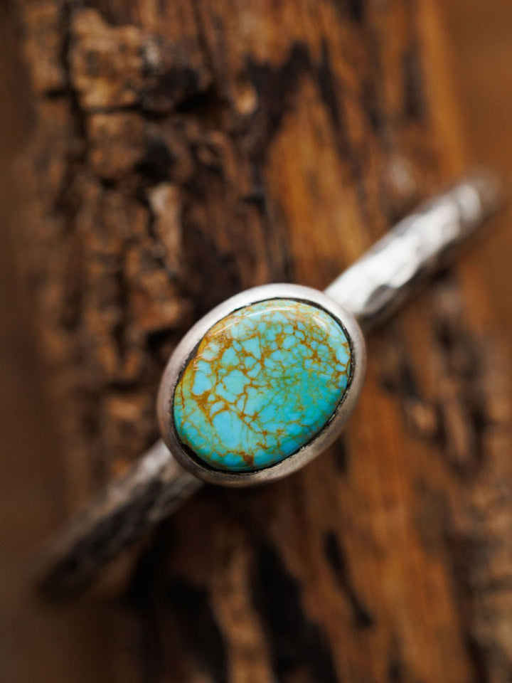 A close-up of the Salida Cuff by Savannah Sevens western life{&}style, a hammered sterling silver cuff with an oval Kings Manassa turquoise stone featuring brown veining, shown resting on textured wood.