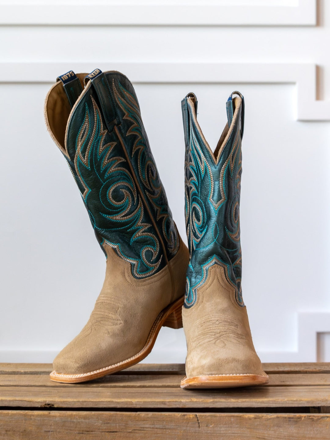 The Hyer Salina Metallic Turquoise Boot by Savannah Sevens western life{&}style, featuring beige leather and teal-blue stitching, stands side by side on a wooden surface against a white background.