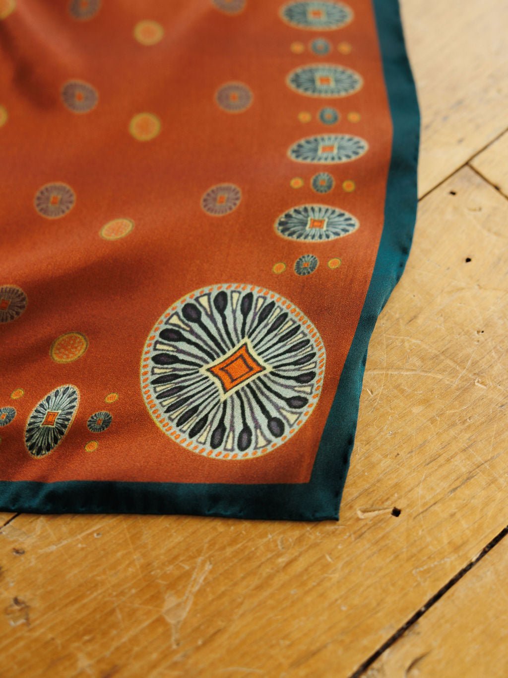 San Miguel Silk Scarf in rust with a dark green border and repeating circular medallions in blue, white, and orange.